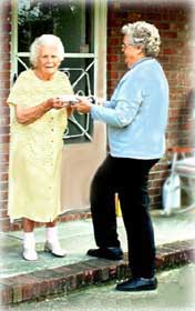 A photograph of a volunteer delivering a meal to a senior at her home.